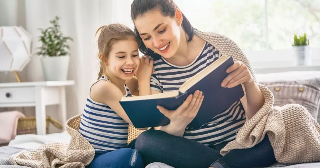Effective Strategies To Improve Your kid's Reading Comprehension Skills 4 A mother and daughter sitting together, smiling and enjoying reading a book in a cozy, brightly lit room, creating a warm and inviting scene.